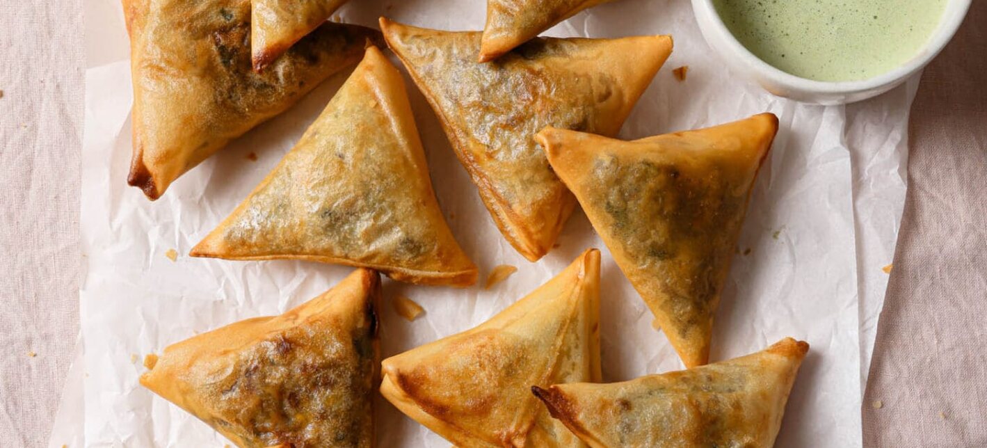Golden samosas on parchment paper with a green chutney dip